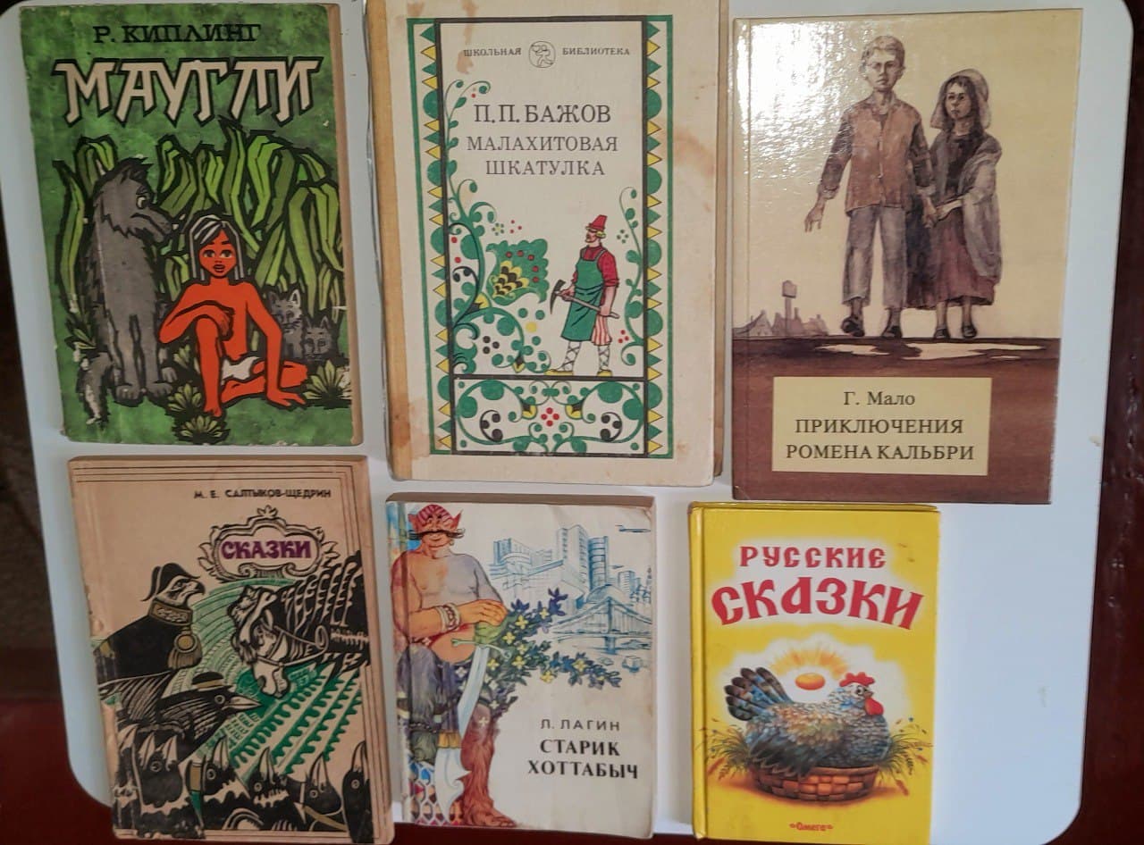 Шесть детских книг с разными обложками, лежащие на белой поверхности.