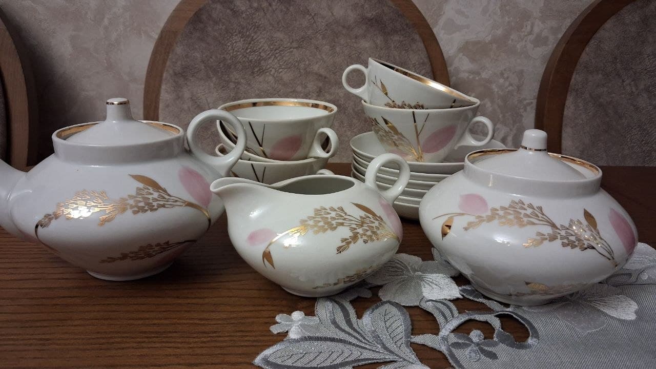 Фарфоровый сервиз с золотисто-розовым узором: чайник, сахарница, молочник, пять чашек и блюдец на столе.