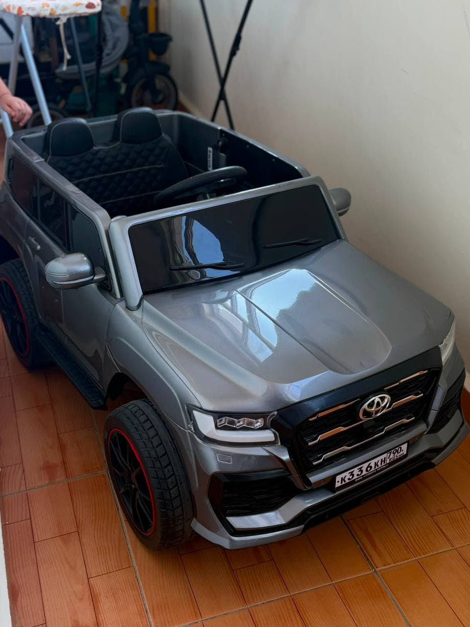 Детская электромашина Land Cruiser серебристого цвета с двумя сиденьями и рулём.