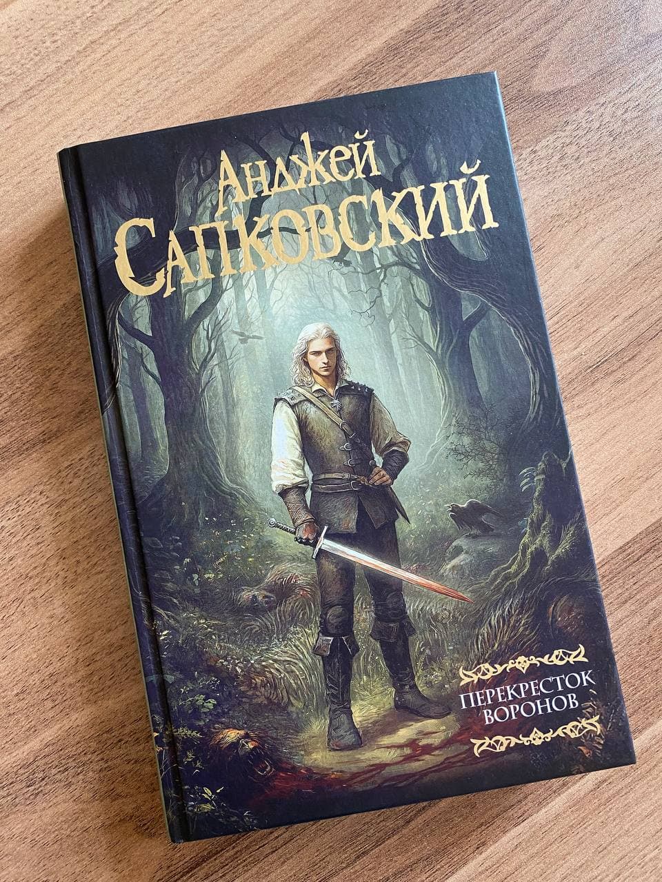 Книга Анджея Сапковского "Перекресток воронов" с изображением персонажа с мечом на фоне леса.