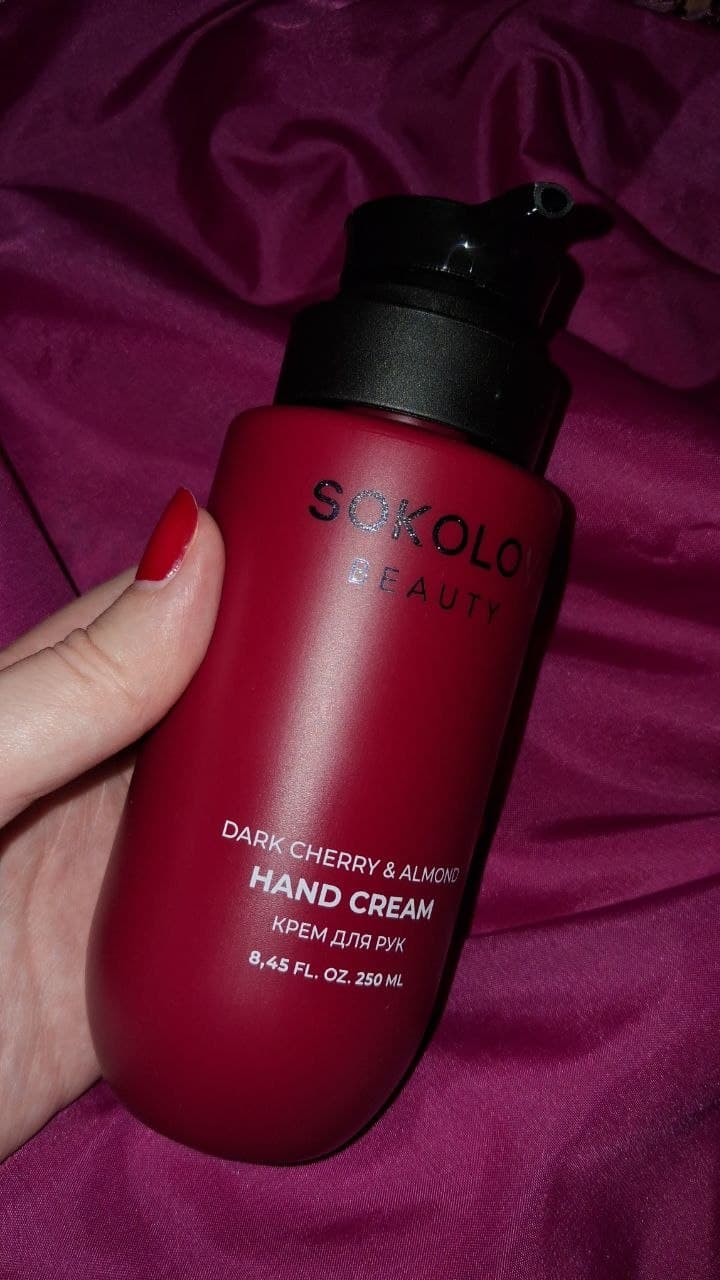 Красная бутылка крема для рук Sokolov Beauty с дозатором на бордовом фоне.