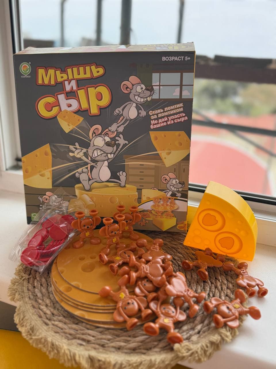 Настольная игра "Мышь и сыр" с фигурками мышей и элементами сыра на фоне коробки игры.
