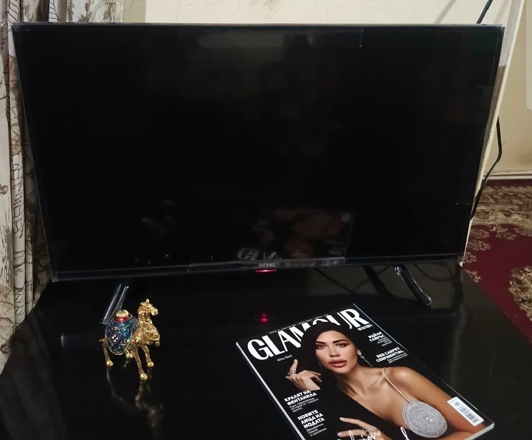 Телевизор на тумбе с журналом Glamour и фигуркой верблюда перед ним.