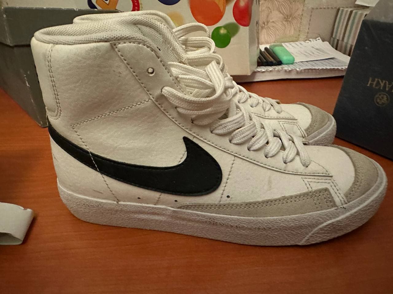 Белые высокие кроссовки Nike Blazer Mid с черным логотипом и надписью NIKE на пятках.