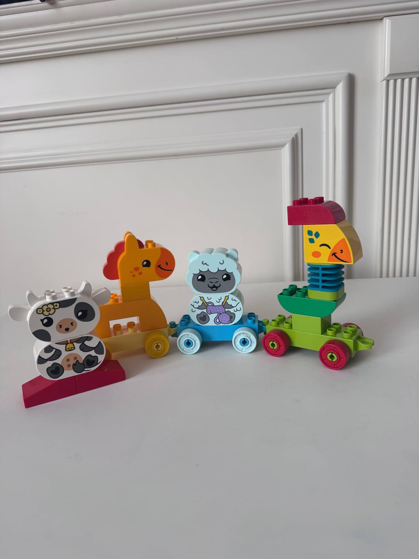 Детали Lego Duplo: животные на колесах и овощи с лицами, красный трактор и кубик.