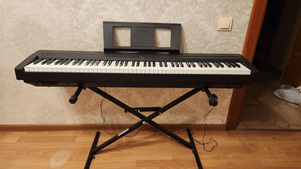 Цифровое пианино Yamaha P-45 на металлической стойке в комнате.