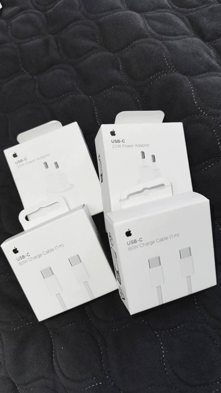 Четыре коробки с оригинальными зарядными адаптерами и кабелями USB-C Apple на темном фоне.