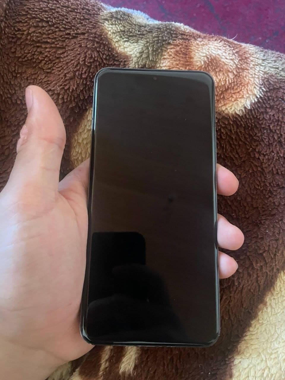 Смартфон Xiaomi 14 Pro черного цвета с выключенным экраном в руке на фоне ткани.