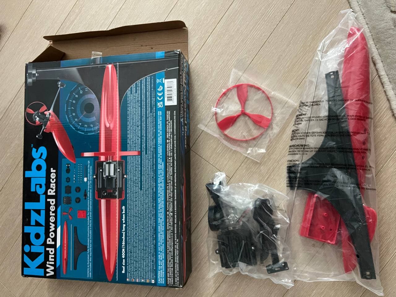 Коробка конструктора KidzLabs Wind Powered Racer и детали в пакетах на светлом полу.