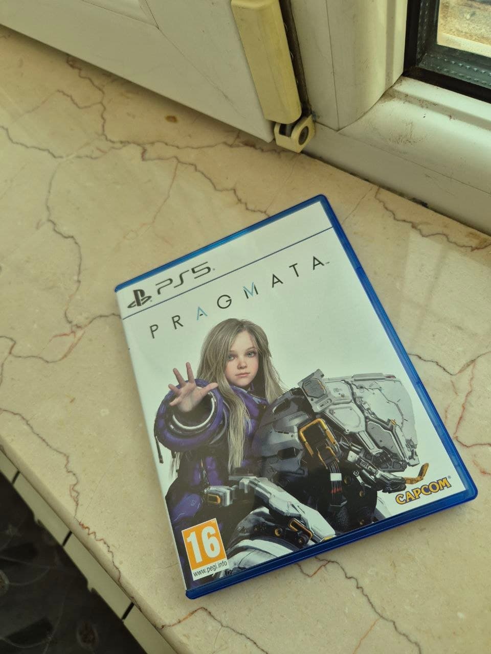 Коробка с игрой PRAGMATA для PS5 на мраморной поверхности.