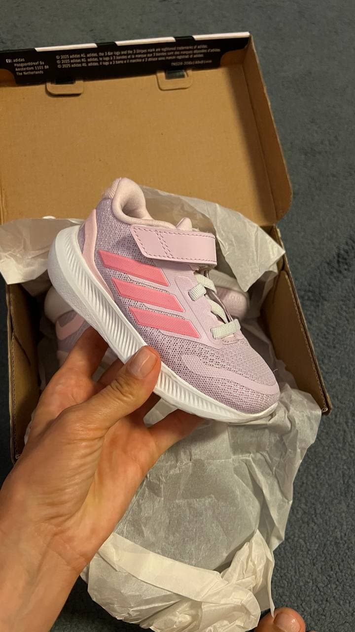 Детская розовая кроссовка Adidas в руке на фоне открытой коробки.