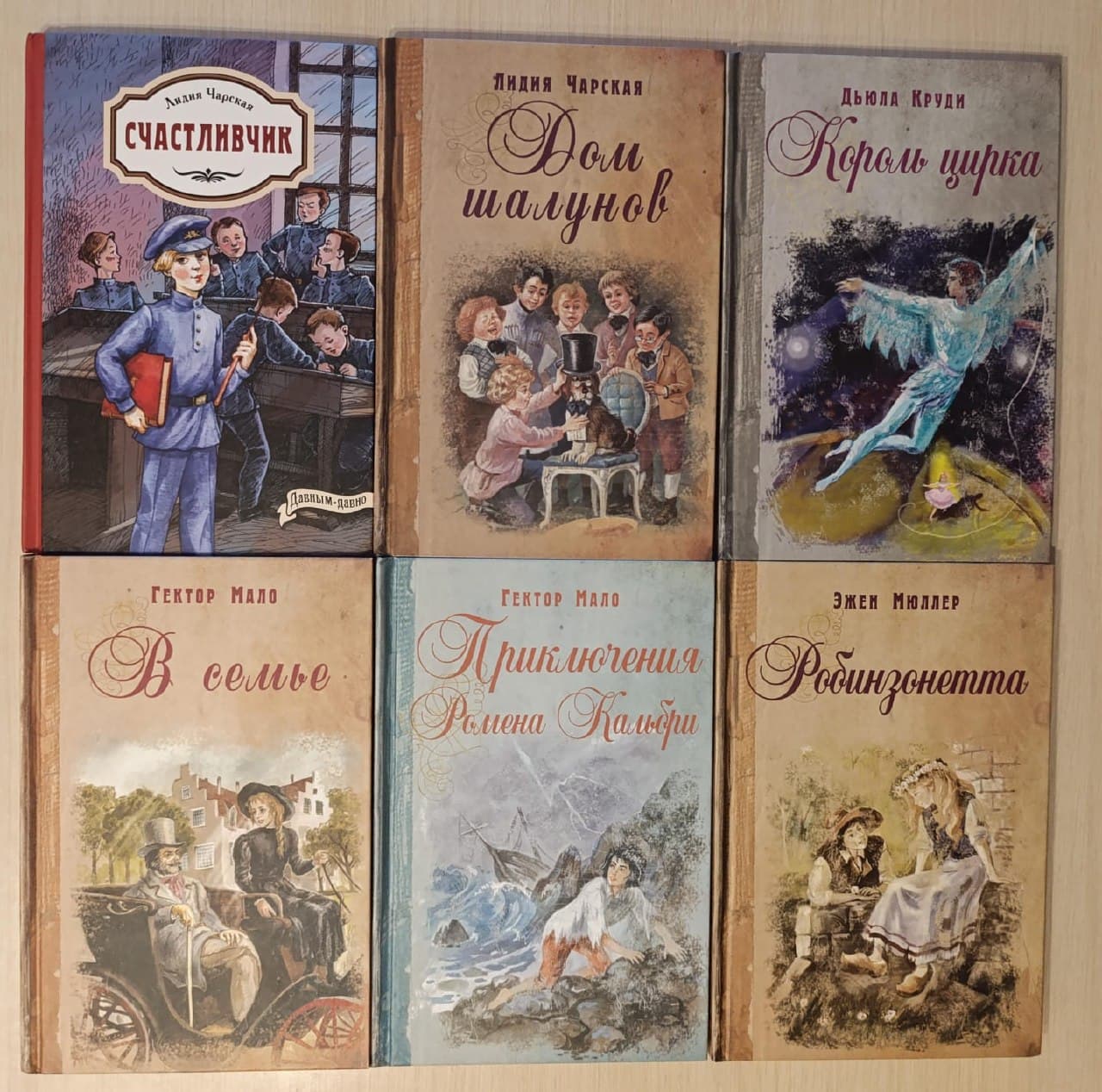 Шесть книг с разными иллюстрированными обложками, выложенные на светлой поверхности.