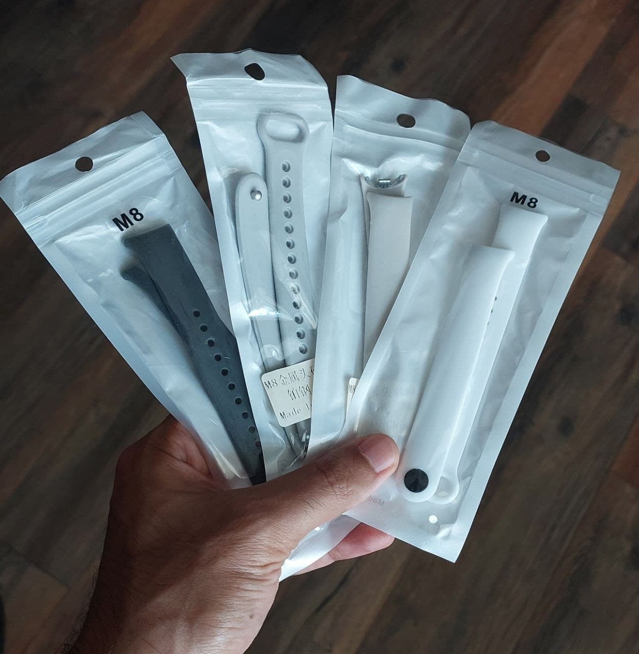Четыре упакованных ремешка для Xiaomi Smartband в руке на фоне деревянного пола.