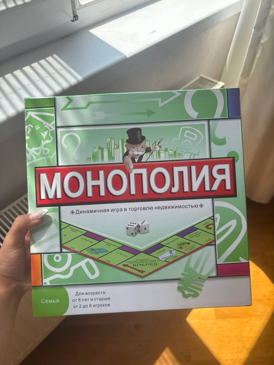 Коробка настольной игры "Монополия" зеленого цвета с надписью и изображением игрового поля.