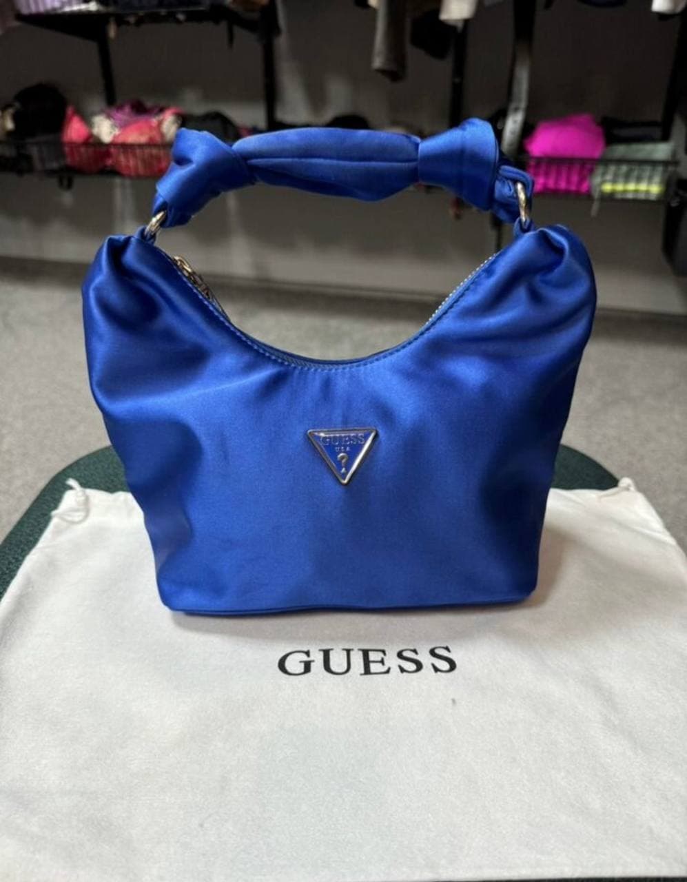 Синяя сумка Guess с короткой ручкой на белом мешке с надписью GUESS.