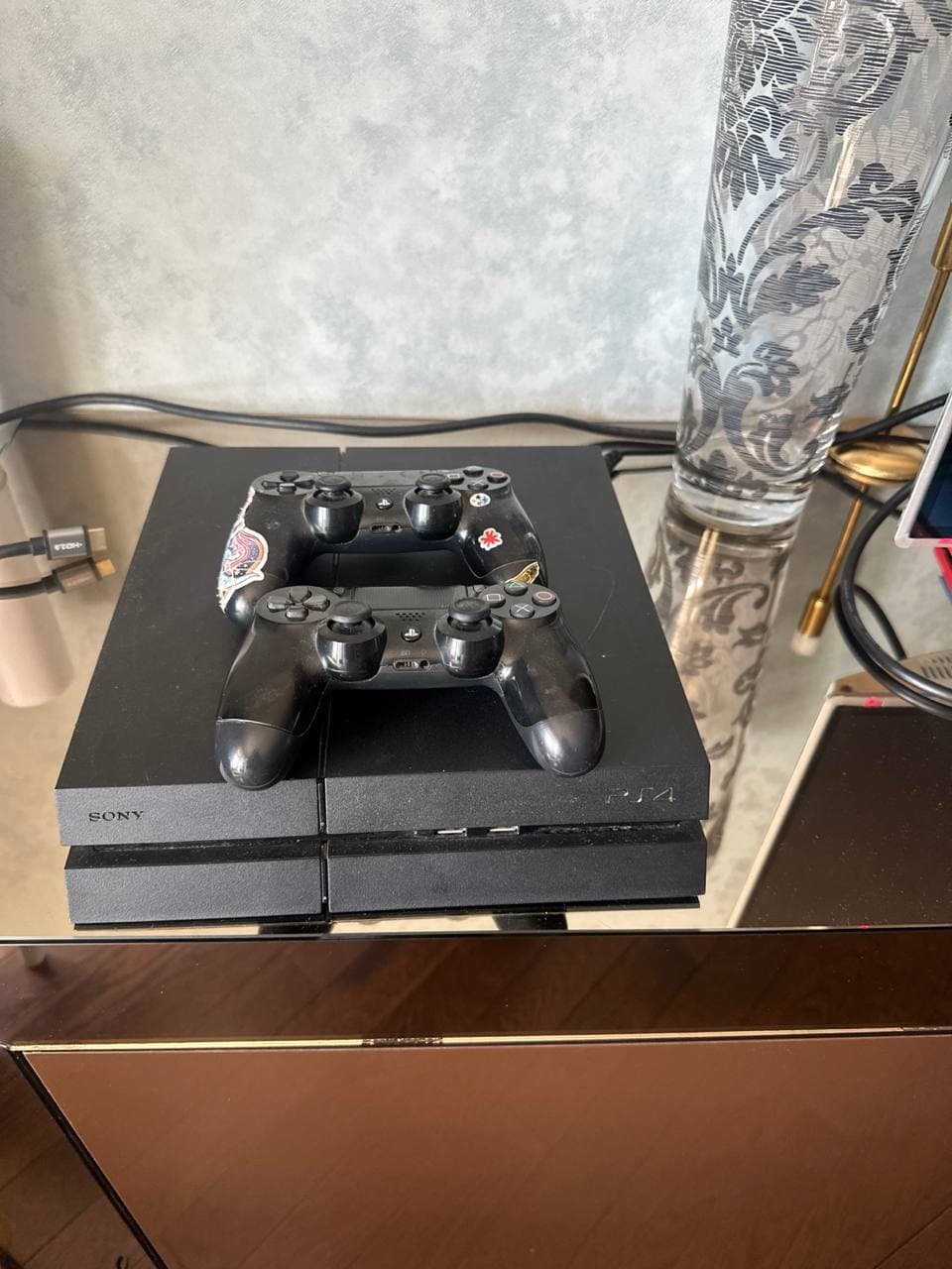Игровая консоль PlayStation 4 с двумя джойстиками на стеклянном столе.