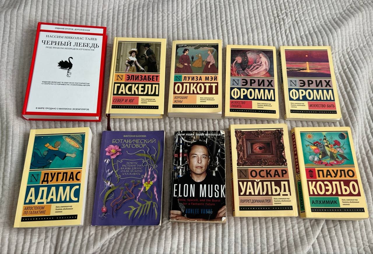 Книги разного жанра и обложек, включая "Черный лебедь" в твердой красной обложке и "Север и Юг" в твердой желтой обложке, разложены на светлой поверхности.