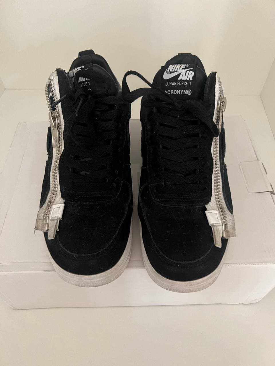 Черные кроссовки Nike Air Lunar Force 1 с белыми молниями и белой подошвой, стоящие на белой коробке.