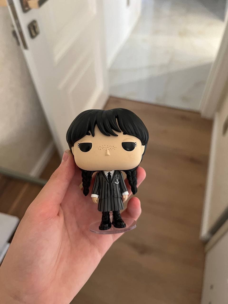 Фигурка Funko Pop персонажа Уэнсдей в школьной форме с косичками, держимая в руке.