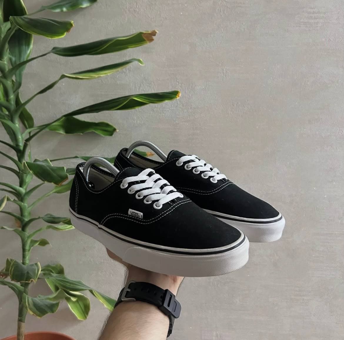 Черные кроссовки Vans с белой подошвой и шнурками, держит рука.