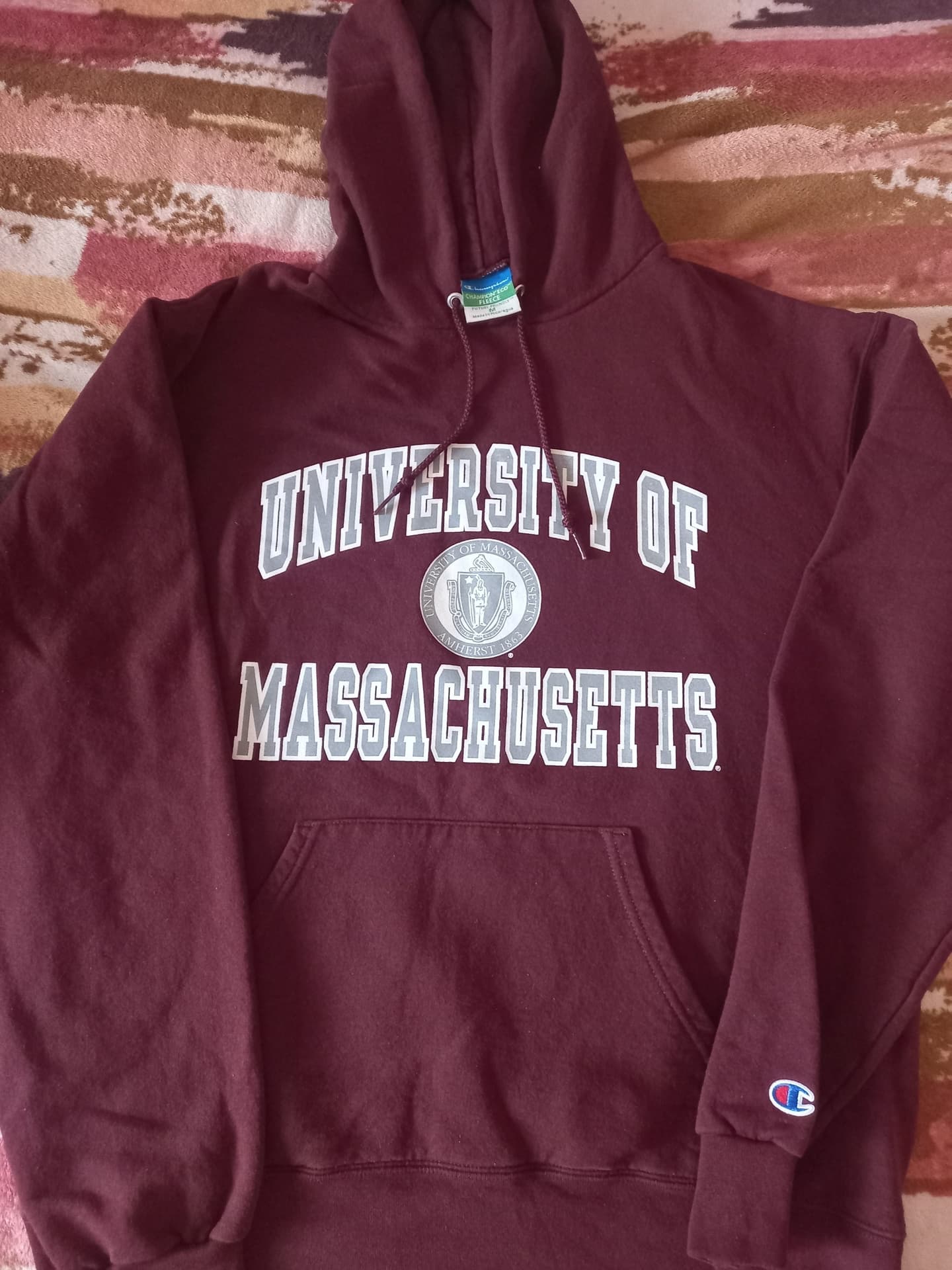 Бордовая толстовка с капюшоном и надписью University of Massachusetts, логотип Champion на рукаве.