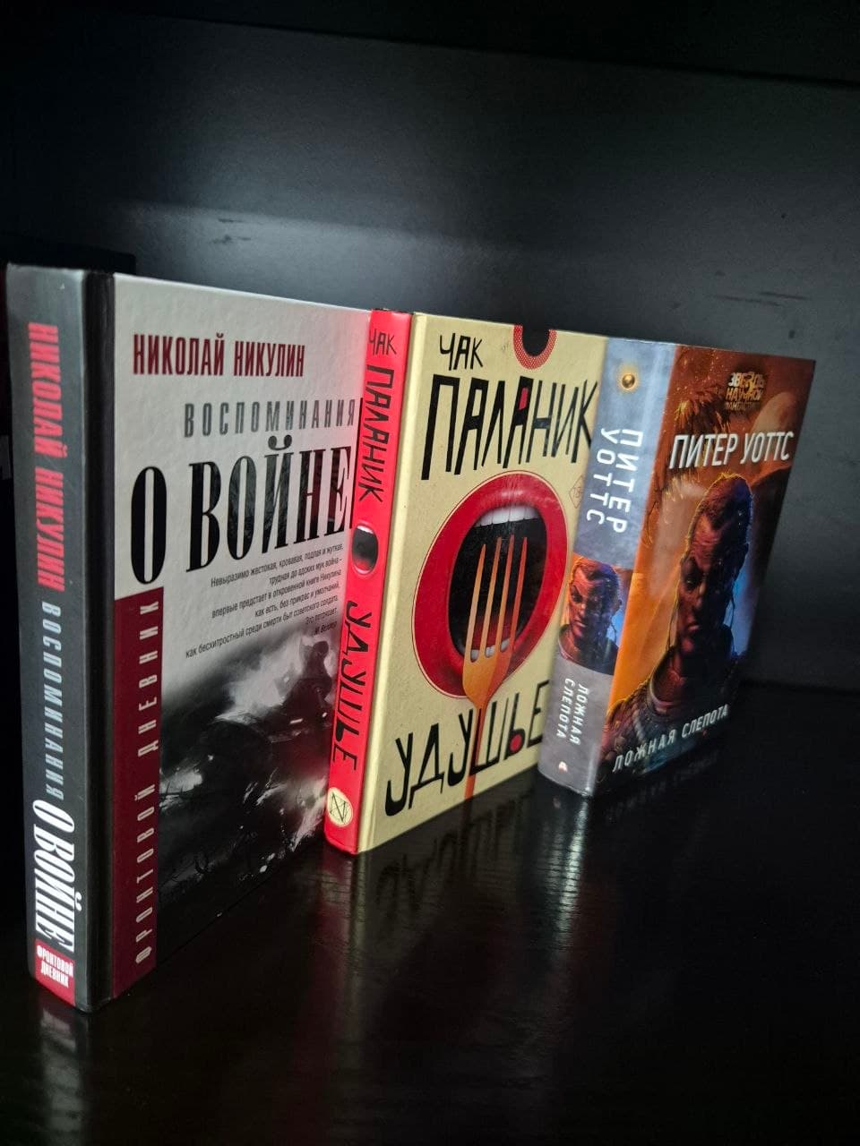 Три книги: "Воспоминания о войне", "Удушье", "Ложная слепота" на темной поверхности.