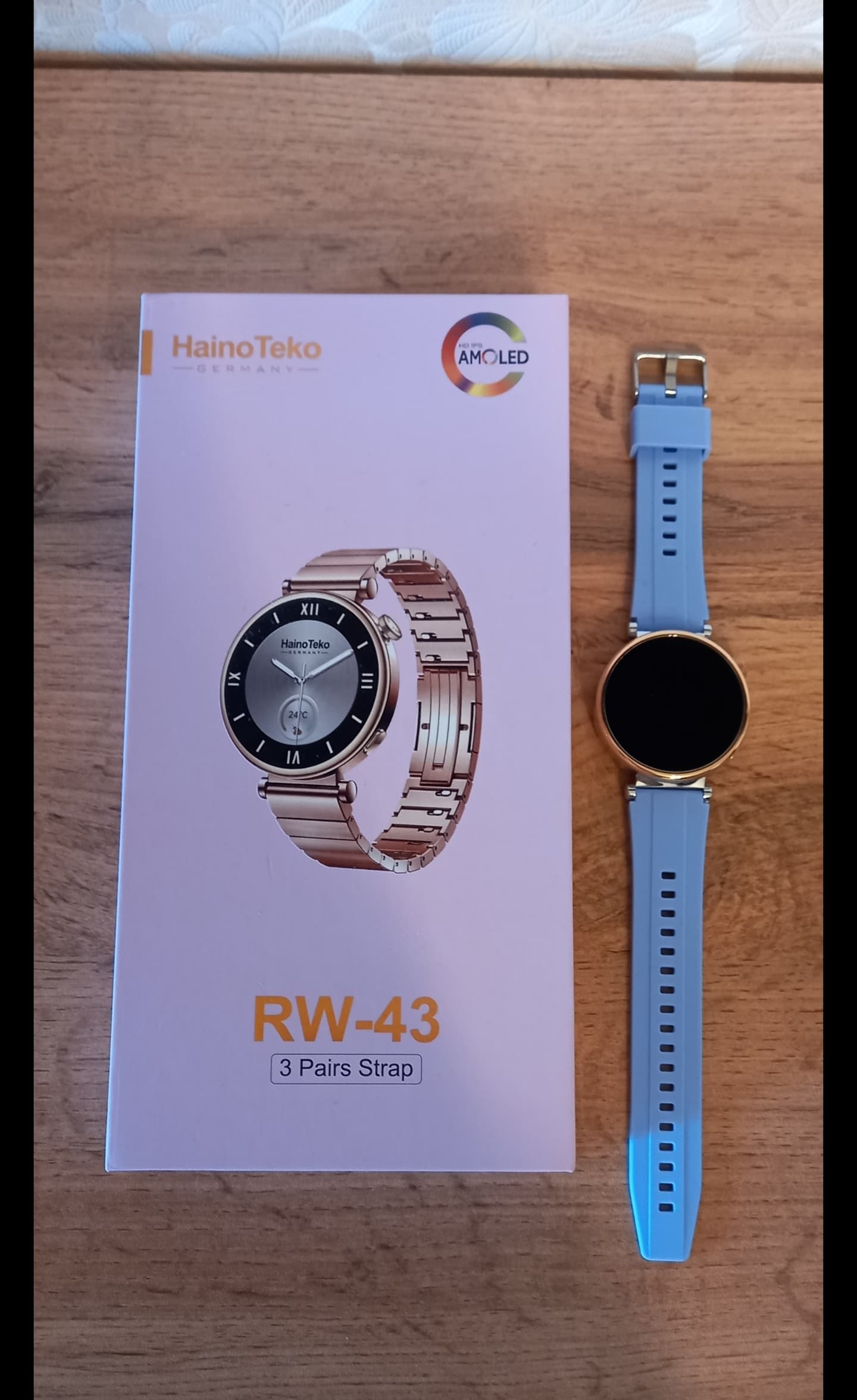 Новые смарт-часы с голубым ремешком и коробка Haino Teko RW-43 на деревянном фоне.