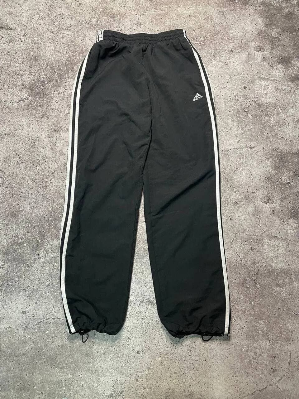 Черные спортивные штаны Adidas с белыми полосками и резинками внизу.