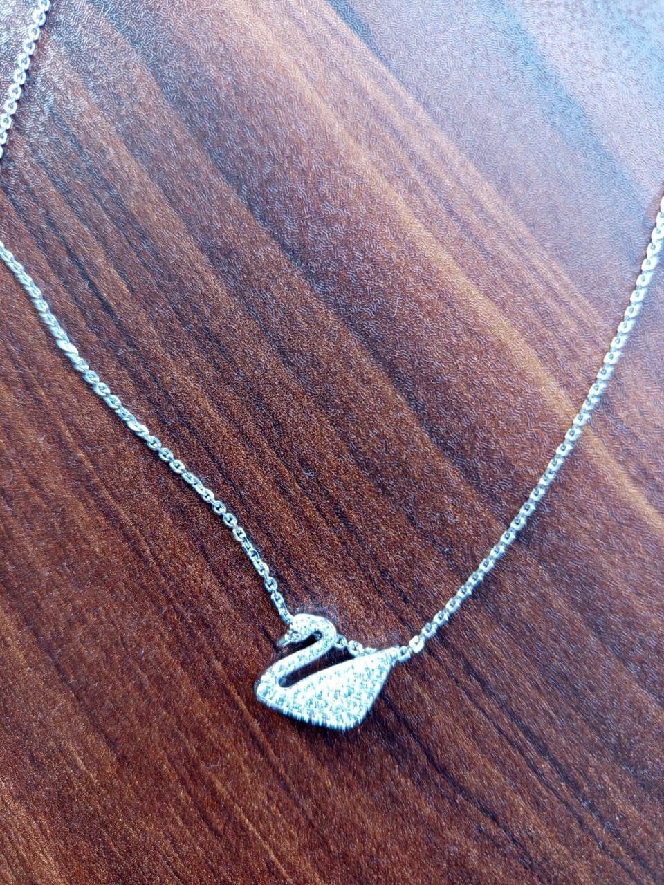 Серебристое колье Swarovski с подвеской в форме лебедя на деревянном фоне.