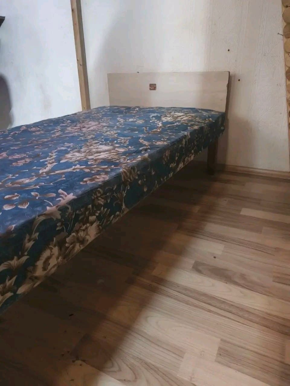 Кровать с деревянным изголовьем и матрасом с цветочным узором.