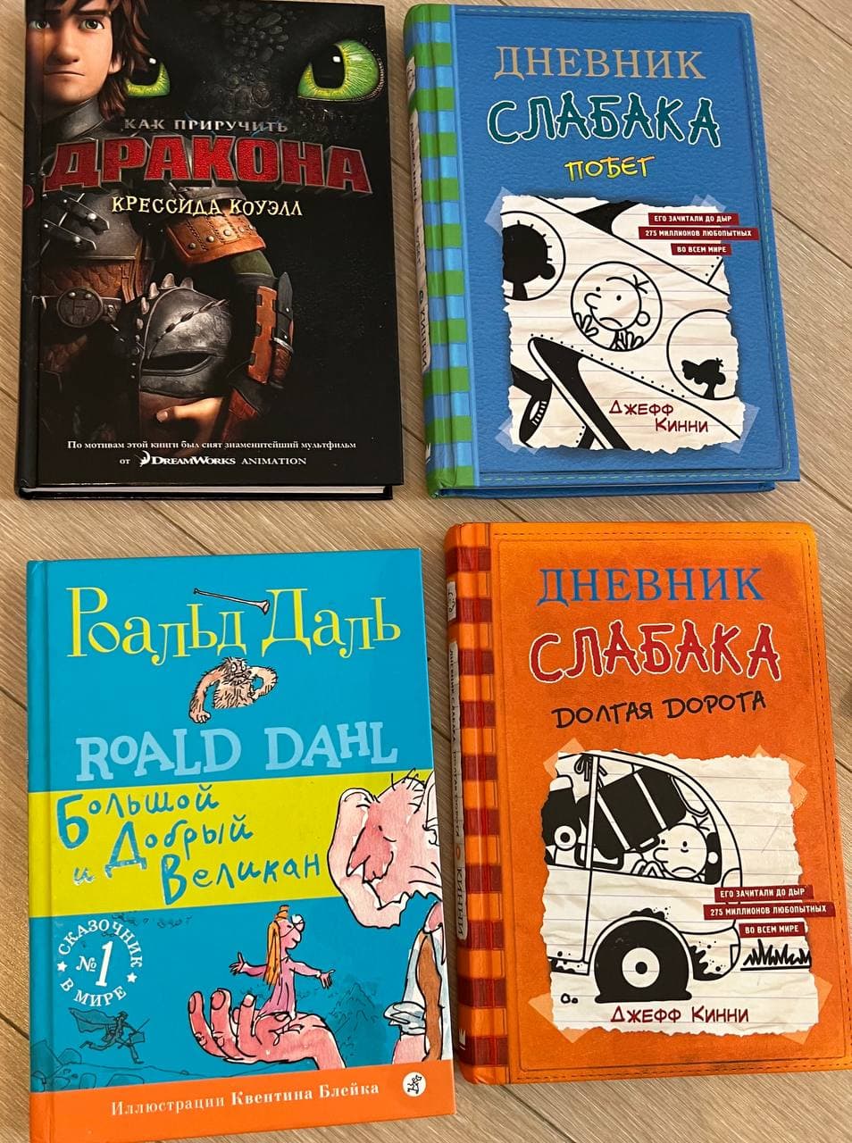 Четыре книги с цветными обложками, лежащие на полу: "Как приручить дракона", две книги "Дневник слабака" и "Большой и добрый великан".